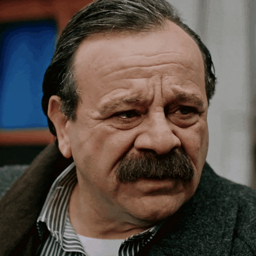 a man with a mustache and a striped shirt is making a sad face