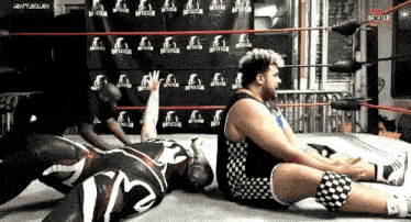 two wrestlers are laying on the floor in a wrestling ring with the words battleclub written on the wall behind them