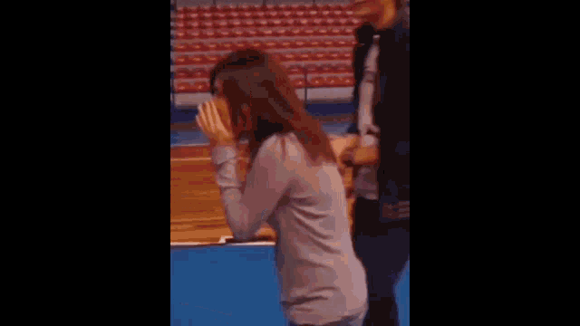 a woman is standing on a basketball court covering her face with her hands .