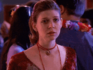 a woman wearing a red necklace with a pendant on it looks at the camera