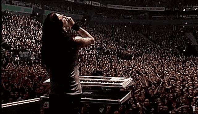 a woman singing into a microphone in front of a crowd with a dell advertisement behind her