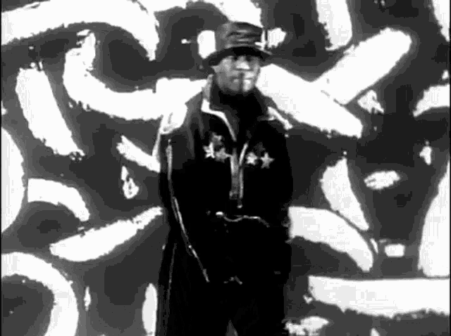 a black and white photo of a man wearing a hat and a jacket .
