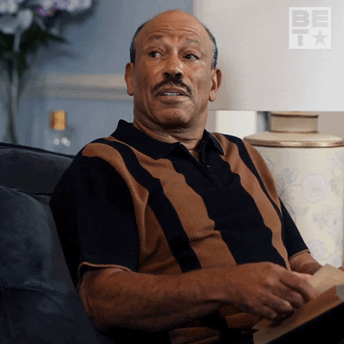 a man sitting on a couch with a lamp and a be tv logo in the corner