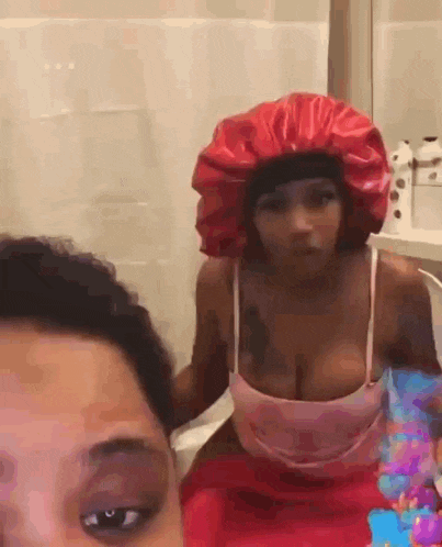 two women are standing next to each other in a bathroom and one of them is wearing a red hat .