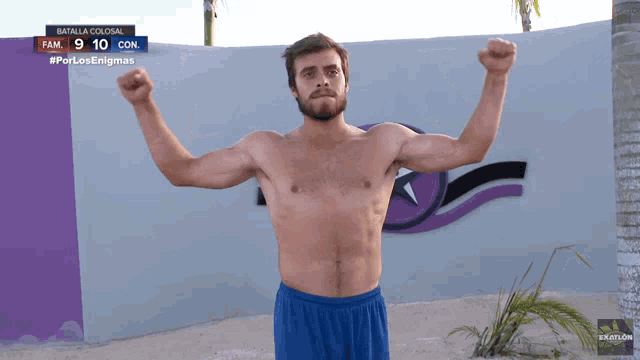 a shirtless man stands in front of a wall that says batalla colosal fame 9 10 con