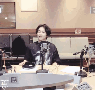a man sitting at a table with a microphone and a sign that says do you like on it