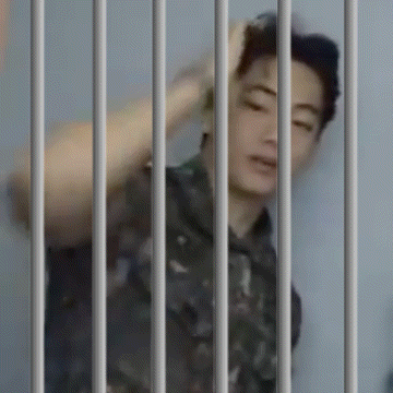 a man in a prison cell behind bars with his hand on his head