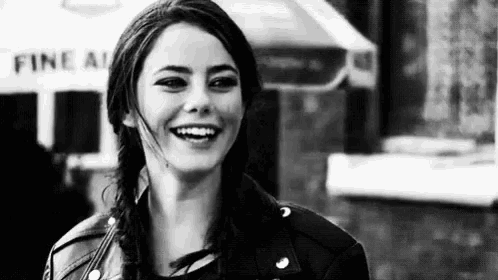 a black and white photo of a woman smiling in front of a building .