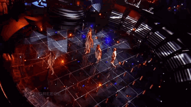 a group of people dancing on a stage with greece written on the bottom right