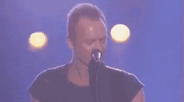 a man is singing into a microphone on a stage while playing a guitar .