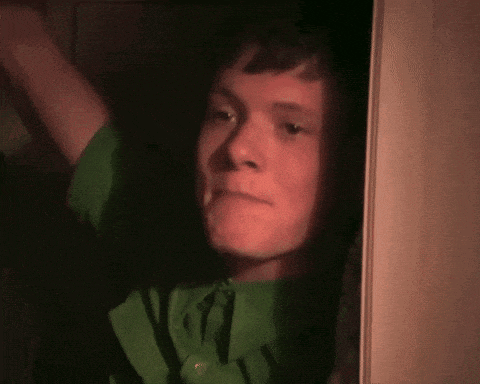 a young man in a green shirt is looking out a doorway