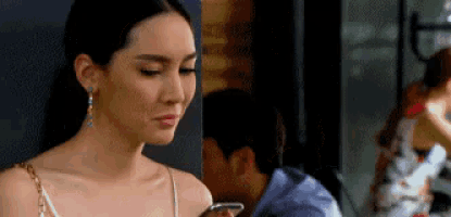 a woman is looking at her cell phone while a man is sitting behind her .