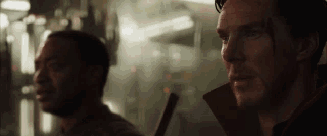 two men are standing next to each other in a dark room and looking at something