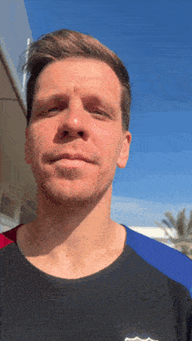 a man wearing a black shirt with a fcb logo on the front looks at the camera