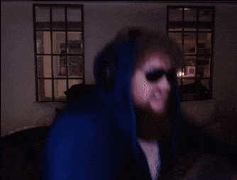 a man in a blue hoodie and sunglasses is dancing in a dark room