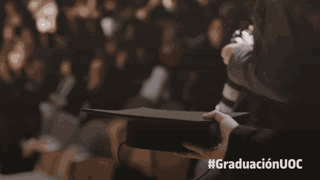 a person holding a graduation cap with the hashtag #graduacionuoc on the bottom right