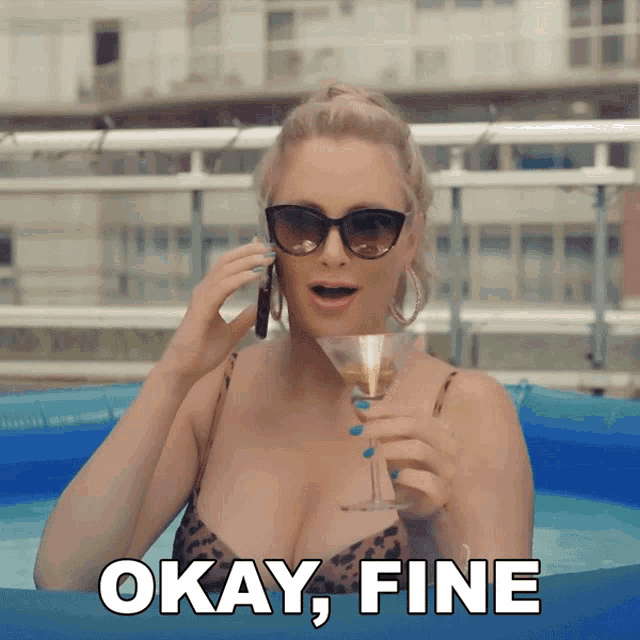 a woman in a bikini is holding a martini and talking on a cell phone with the words " okay fine " behind her