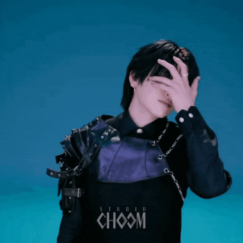 a man in a black and purple outfit is covering his face with his hands in front of a studio choom logo