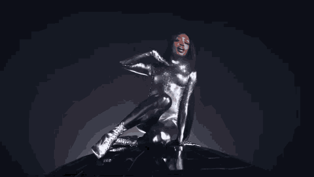 a woman in a silver bodysuit sits on a black object