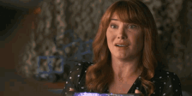 a woman with red hair and a necklace with a heart on it looks surprised