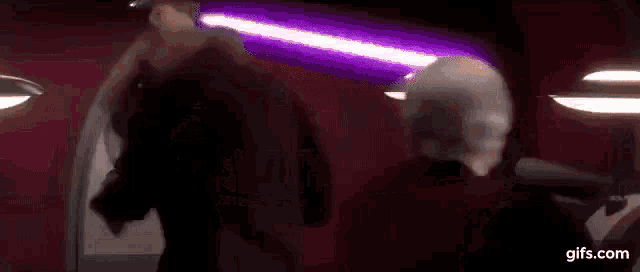 a group of people are standing next to each other in a dark room with lightsabers in the background .