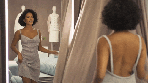a woman is standing in front of a mirror wearing a silver dress