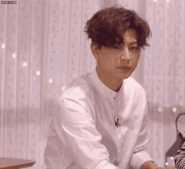 a young man in a white shirt is making a heart shape with his hands