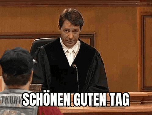 a man in a judge 's robe is sitting in a courtroom with a man in a baseball cap .