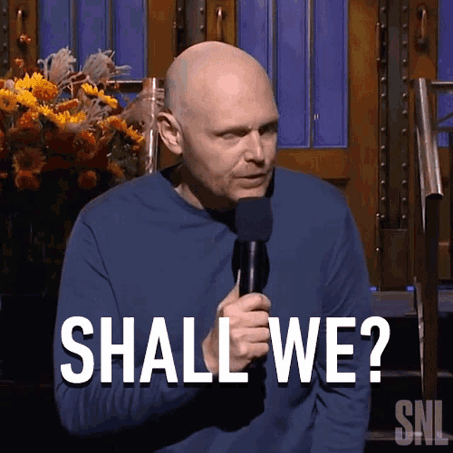 a man holding a microphone with the words shall we written above him