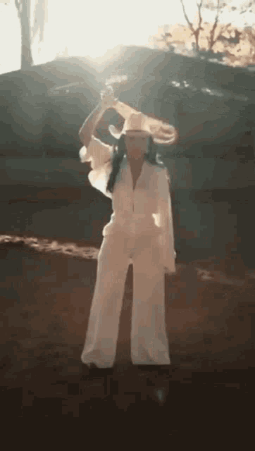 a woman wearing a cowboy hat and a white jumpsuit is dancing in the desert .