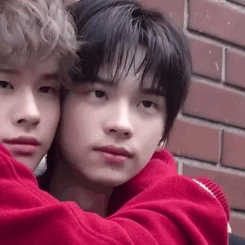 two young men are hugging each other while standing next to each other in front of a brick wall .