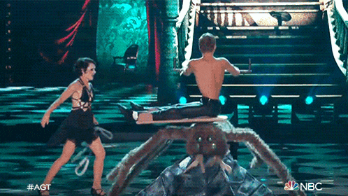a man is sitting on a giant spider while a woman stands nearby