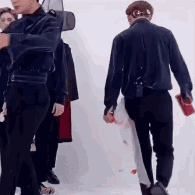 a group of men are standing next to each other in a room . one of the men is holding a red bag .