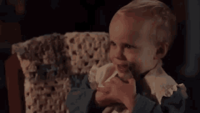 a baby is sitting in a chair with a stuffed animal in his hand .
