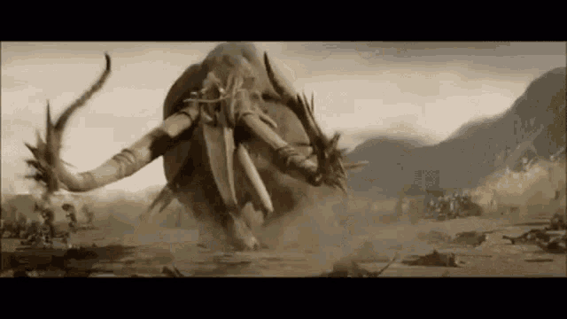 a giant elephant is standing in the middle of a field with a mountain in the background .