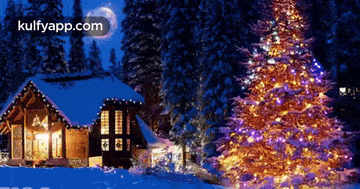 a christmas tree is lit up in front of a snowy cabin