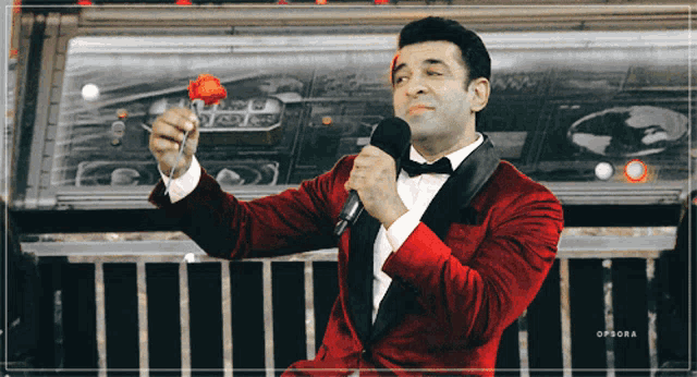 a man in a red tuxedo is holding a red rose and a microphone
