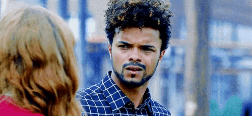 a man with curly hair and a beard is talking to a woman in a red shirt .