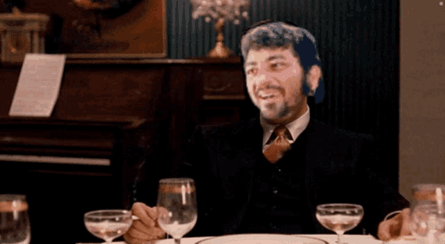 a man in a suit and tie sits at a table with two glasses of wine