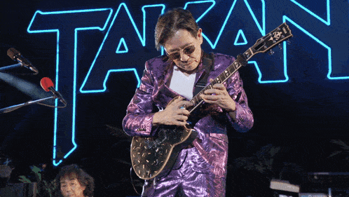a man in a purple suit is playing a guitar in front of a neon sign that says taran