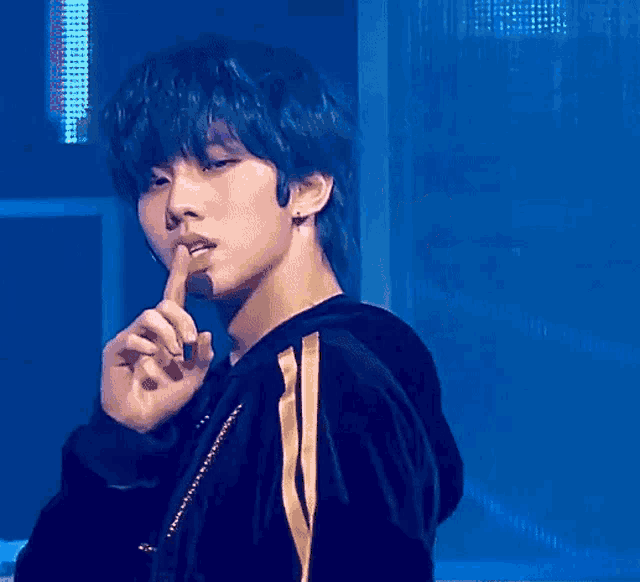 a young man with blue hair holds his finger to his lips
