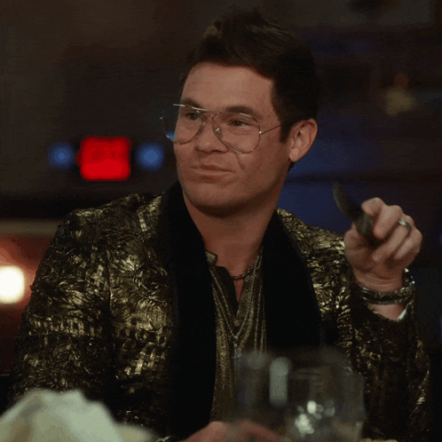 a man with glasses and a gold jacket is holding a knife and fork