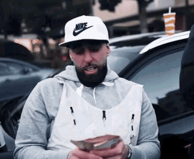 a man wearing a white nike hat is holding a bunch of money