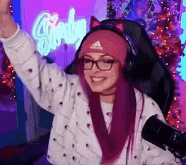 a woman with purple hair and glasses is wearing headphones and a pink hat .