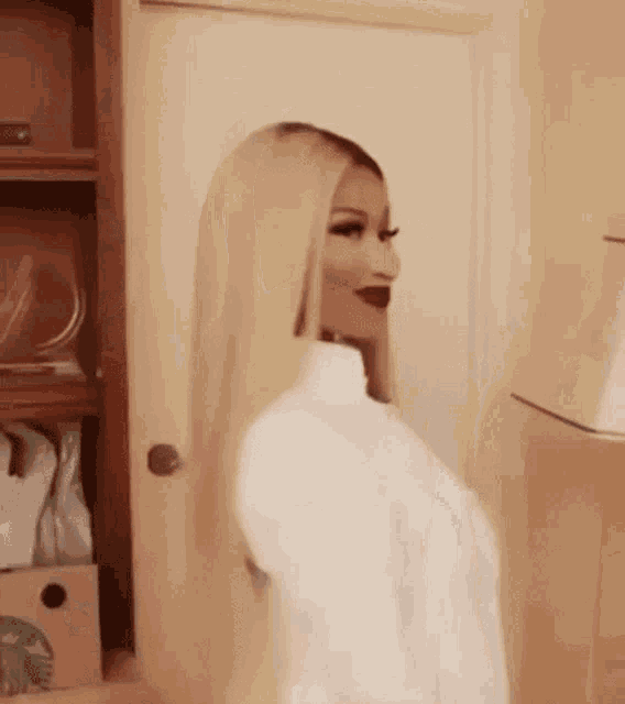 a woman with long blonde hair and red lipstick is standing in front of a door in a room .