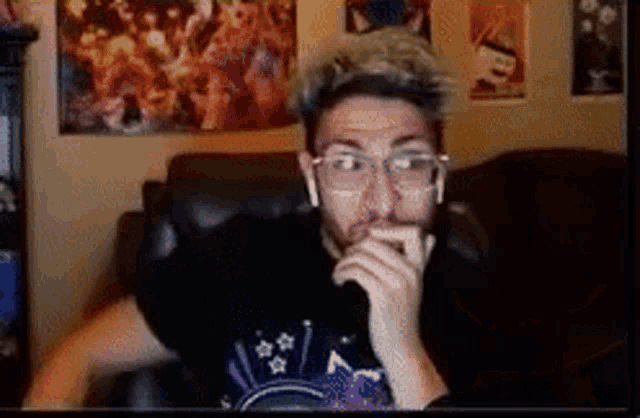 a man wearing glasses and ear buds is sitting in a chair in front of a computer screen .