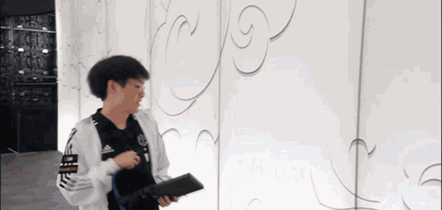 a man is standing in front of a white wall and holding a laptop .