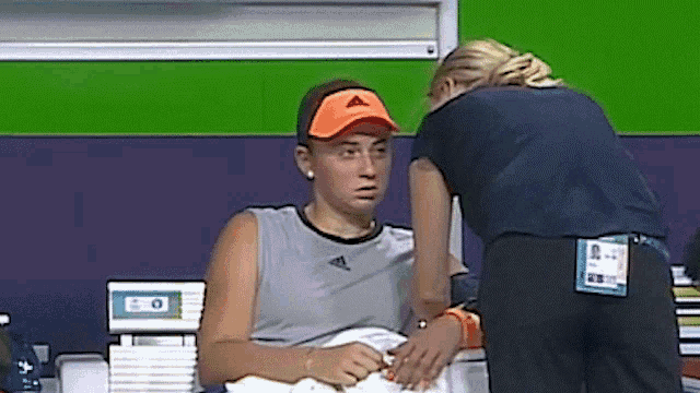 a woman wearing an orange adidas hat is sitting in a chair