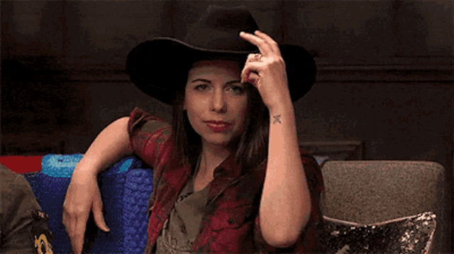 a woman wearing a cowboy hat is sitting on a couch with her hand on her hat .
