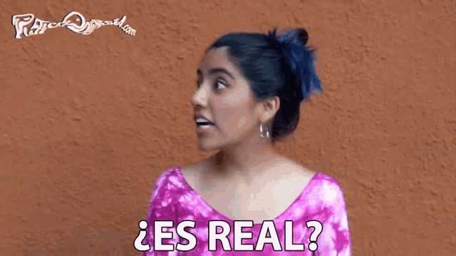a woman in a pink shirt is smiling and says " es real "
